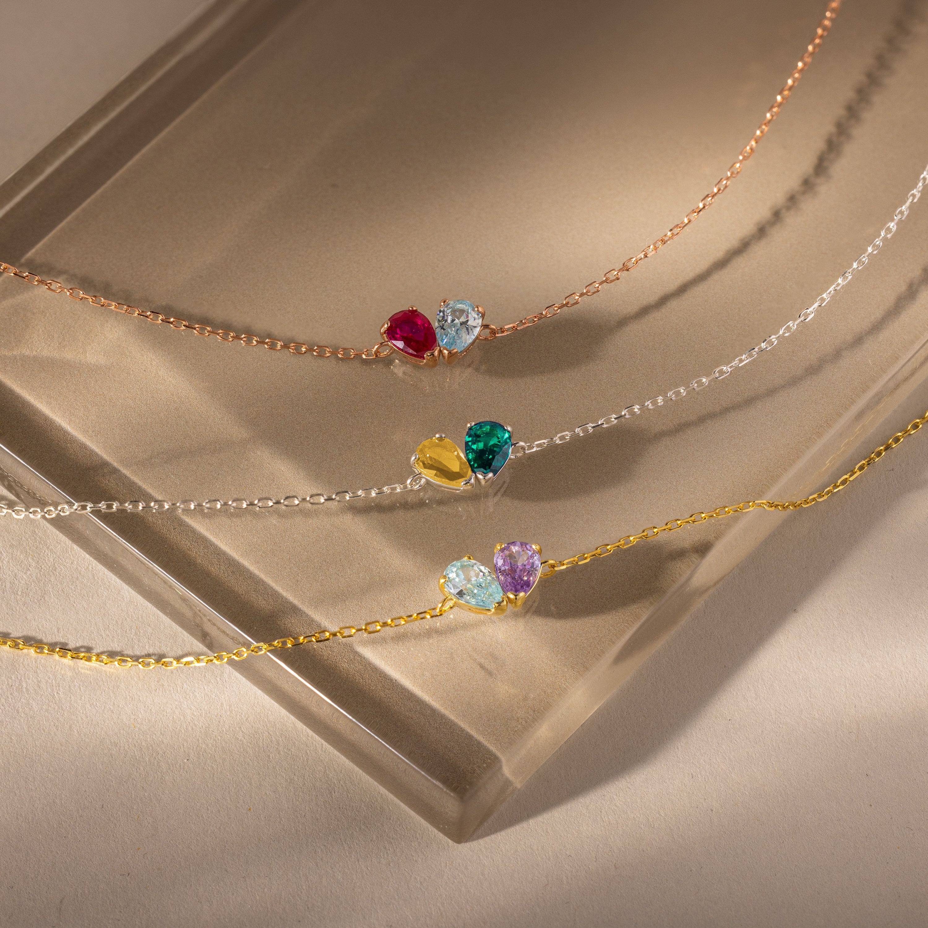 The Toi et Moi Teardrop Heart Bracelet, featuring a colorful gemstone heart pendant that shimmers like a pear-cut stone, rests elegantly on a frosted glass surface.