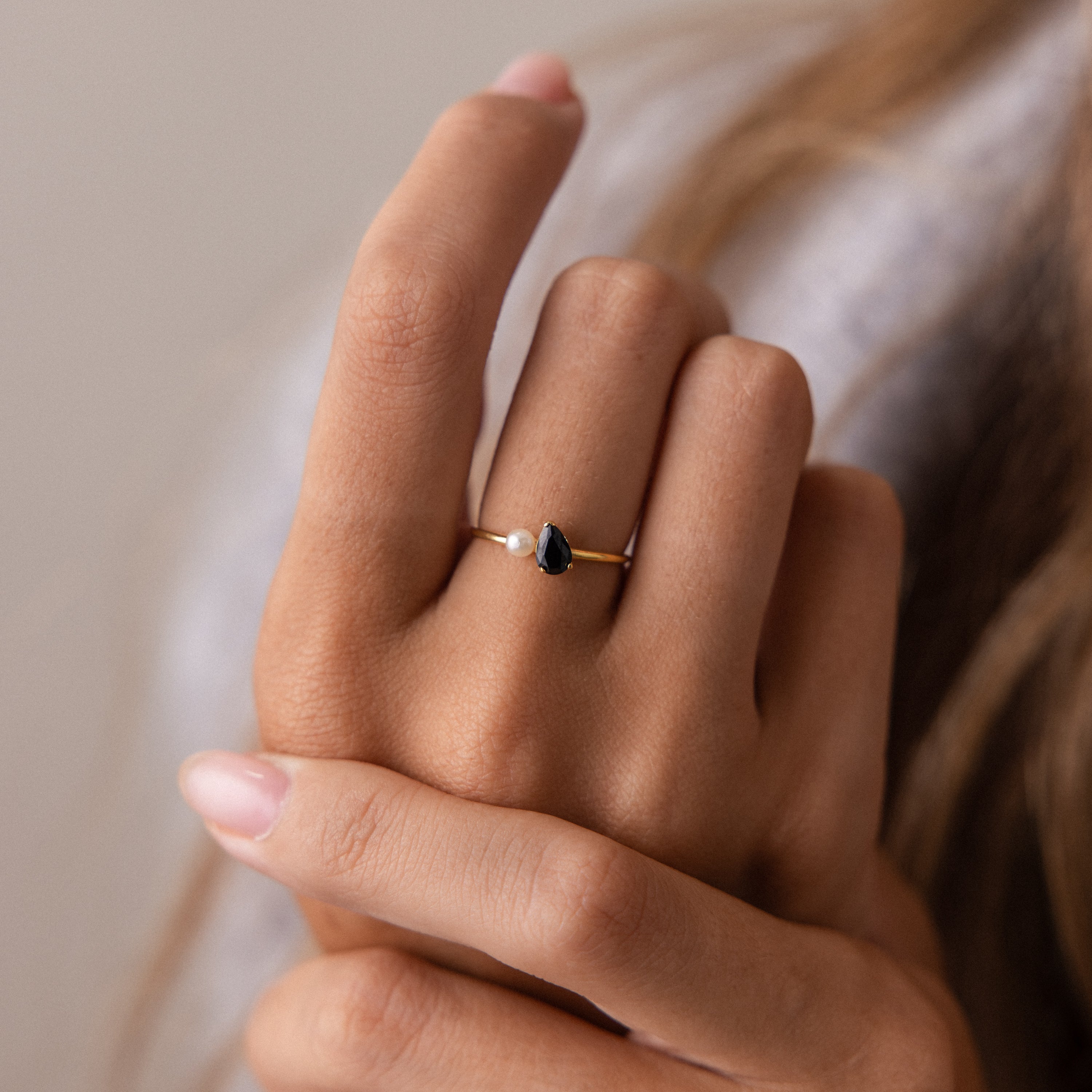 A hand displays the Teardrop Birthstone & Pearl Ring—featuring a February amethyst gem and pearl—elegantly shining on the ring finger.