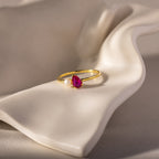 The Teardrop Ruby & Pearl Ring, featuring a radiant red gemstone and a lustrous pearl, rests on a white, wavy ceramic surface—a true symbol of elegance.