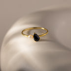 The Teardrop Onyx & Pearl Ring, featuring a black teardrop onyx and a lustrous pearl, rests on a smooth white surface, showcasing the essence of elegant jewelry.