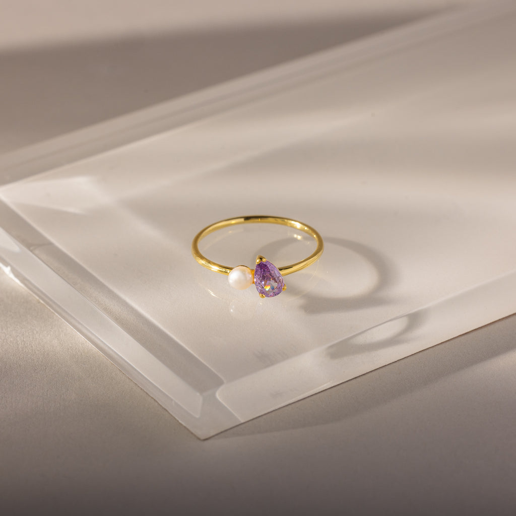 Teardrop Alexandrite & Pearl Ring: Gold ring with a teardrop alexandrite birthstone and a small white pearl, beautifully displayed on a clear, angled acrylic surface.