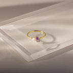 Teardrop Alexandrite & Pearl Ring: Gold ring with a teardrop alexandrite birthstone and a small white pearl, beautifully displayed on a clear, angled acrylic surface.