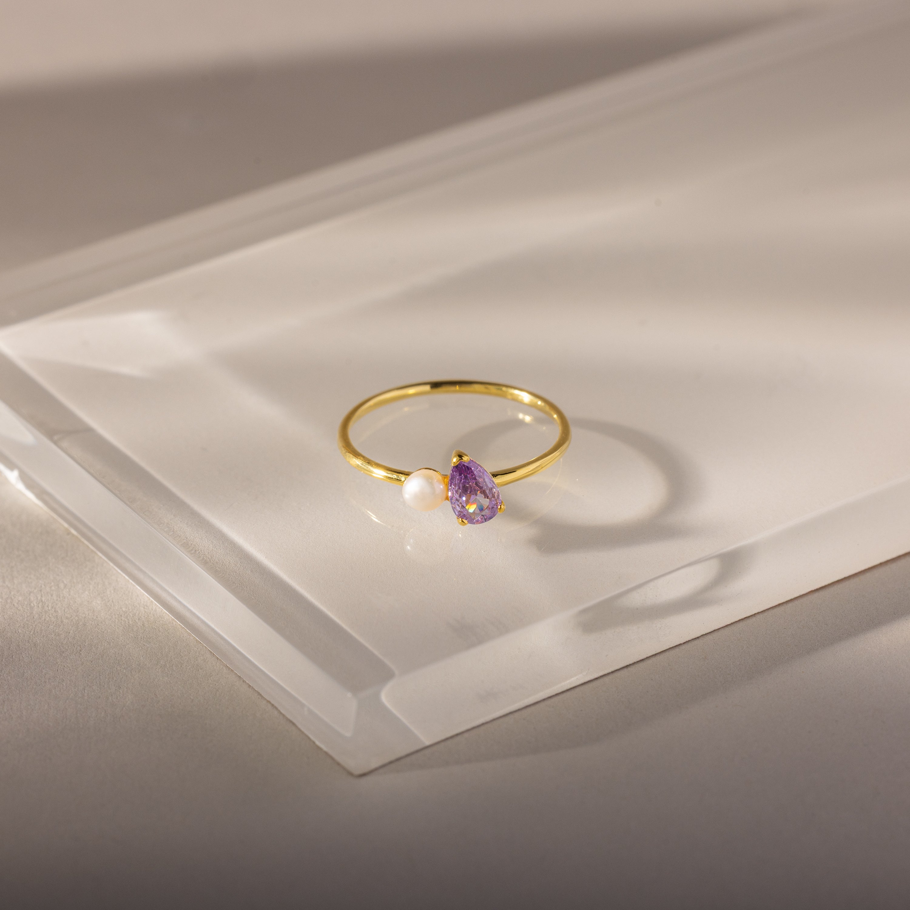 Teardrop Alexandrite & Pearl Ring: Gold ring with a teardrop alexandrite birthstone and a small white pearl, beautifully displayed on a clear, angled acrylic surface.