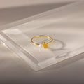 The Teardrop Topaz & Pearl Ring, featuring a yellow topaz and a white pearl, sits on a translucent surface, highlighting elegant jewelry perfect for any occasion.