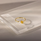 The Teardrop Topaz & Pearl Ring, featuring a yellow topaz and a white pearl, sits on a translucent surface, highlighting elegant jewelry perfect for any occasion.