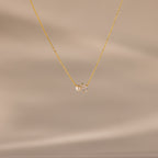 The Teardrop Diamond & Pearl Necklace features a delicate gold chain with a pearl and clear gemstone pendant, shown on a soft beige background—an elegant gift for any occasion.