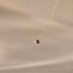 Teardrop Amethyst & Pearl Necklace featuring a gold chain, a delicate white pearl, and an amethyst teardrop pendant—an elegant gift for life's milestones, showcased against a soft beige background.