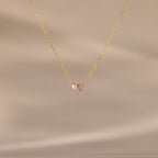 The Teardrop Pink Tourmaline & Pearl Necklace features a delicate gold teardrop pendant with a pink gemstone and pearl, set against a soft beige background—a timeless gift for any occasion.