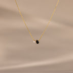 The Teardrop Onyx & Pearl Necklace features a gold chain with a delicate white pearl and black teardrop onyx pendant, displayed on a neutral beige background—an elegant, timeless gift for any occasion.