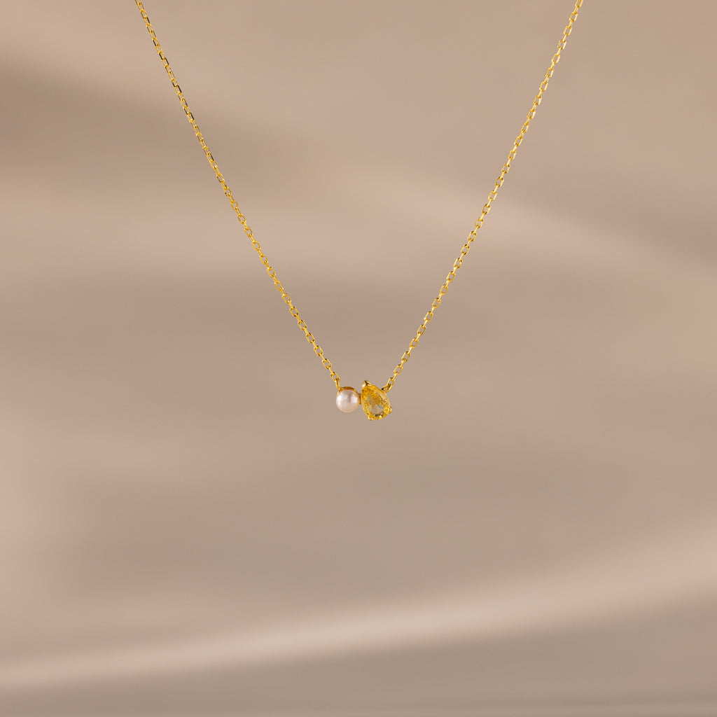 The Teardrop Topaz & Pearl Necklace features a gold chain with a small pearl and yellow topaz teardrop pendant, beautifully displayed on a neutral background—a timeless gift for any occasion.