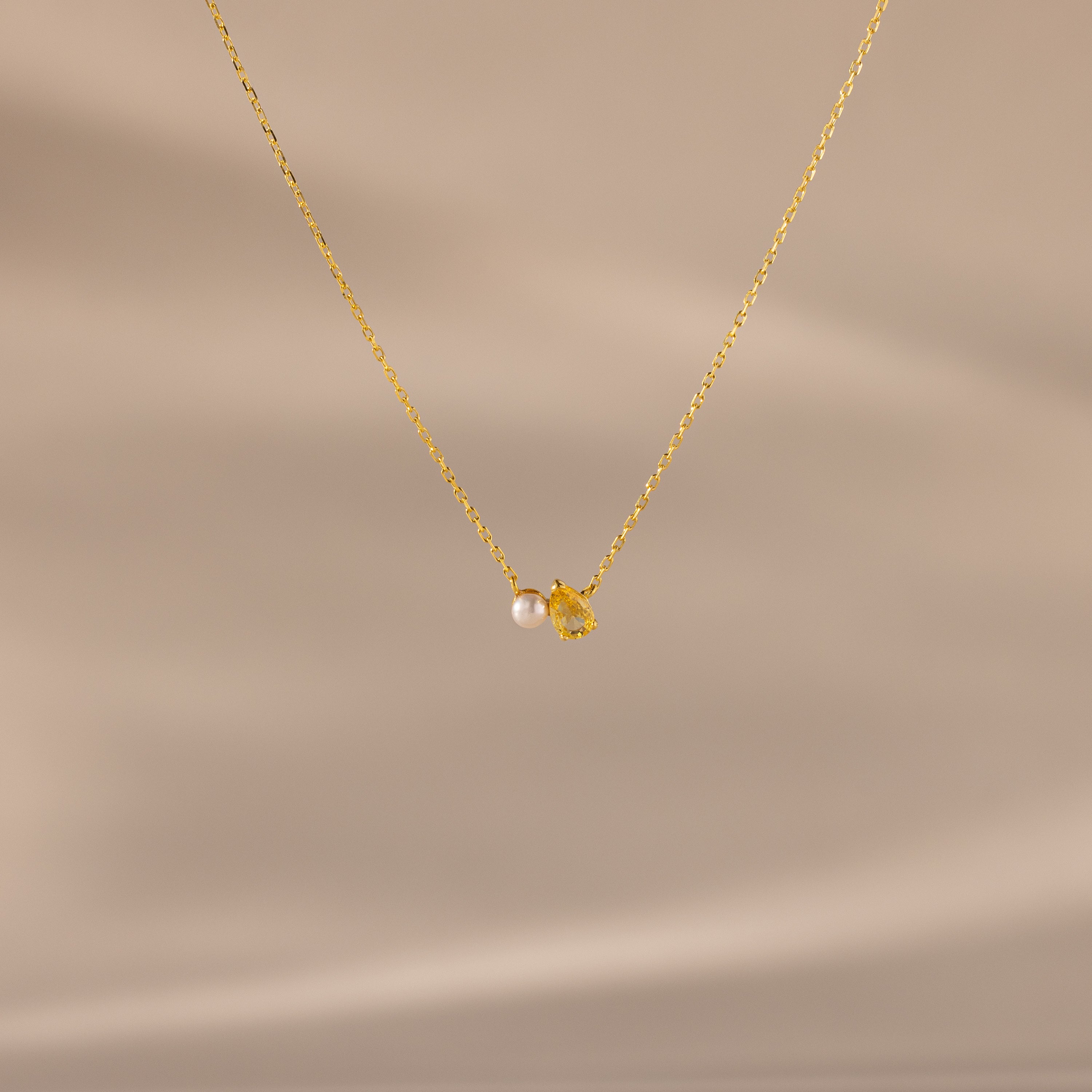 The Teardrop Topaz & Pearl Necklace features a gold chain with a small pearl and yellow topaz teardrop pendant, beautifully displayed on a neutral background—a timeless gift for any occasion.