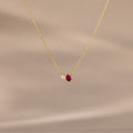 The Teardrop Ruby & Pearl Necklace showcases a delicate pearl and red teardrop birthstone pendant on a soft beige backdrop—perfect for celebrating milestones.