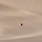The Teardrop Ruby & Pearl Necklace showcases a delicate pearl and red teardrop birthstone pendant on a soft beige backdrop—perfect for celebrating milestones.