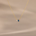 Teardrop Blue Zircon & Pearl Necklace with a small pearl and blue zircon pendant, ideal as a milestone gift, showcased on a soft beige background.