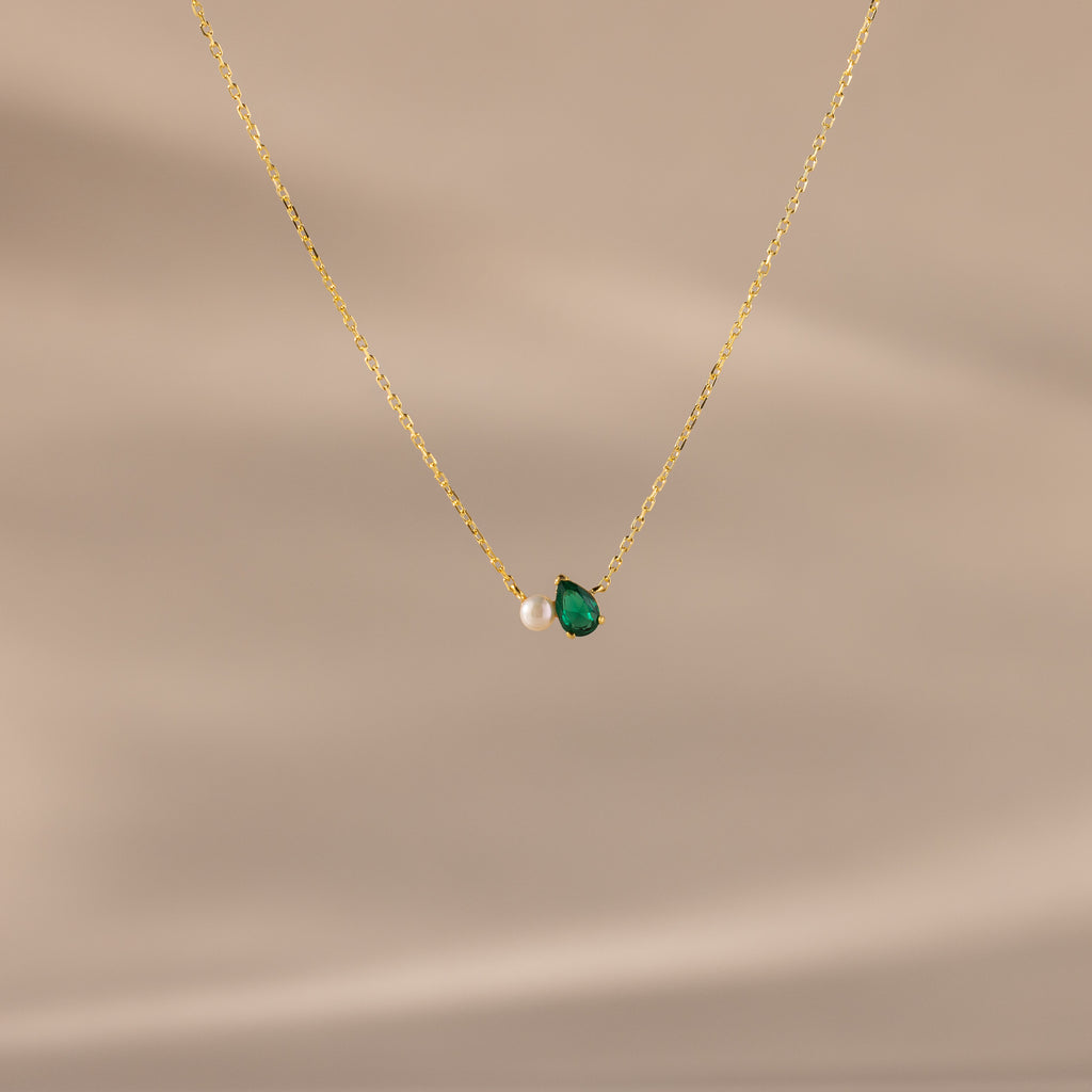 Teardrop Emerald & Pearl Necklace displayed on a beige background. This gold chain pearl necklace with a green teardrop pendant makes a timeless gift, perfect for any occasion.