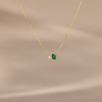 Teardrop Emerald & Pearl Necklace displayed on a beige background. This gold chain pearl necklace with a green teardrop pendant makes a timeless gift, perfect for any occasion.