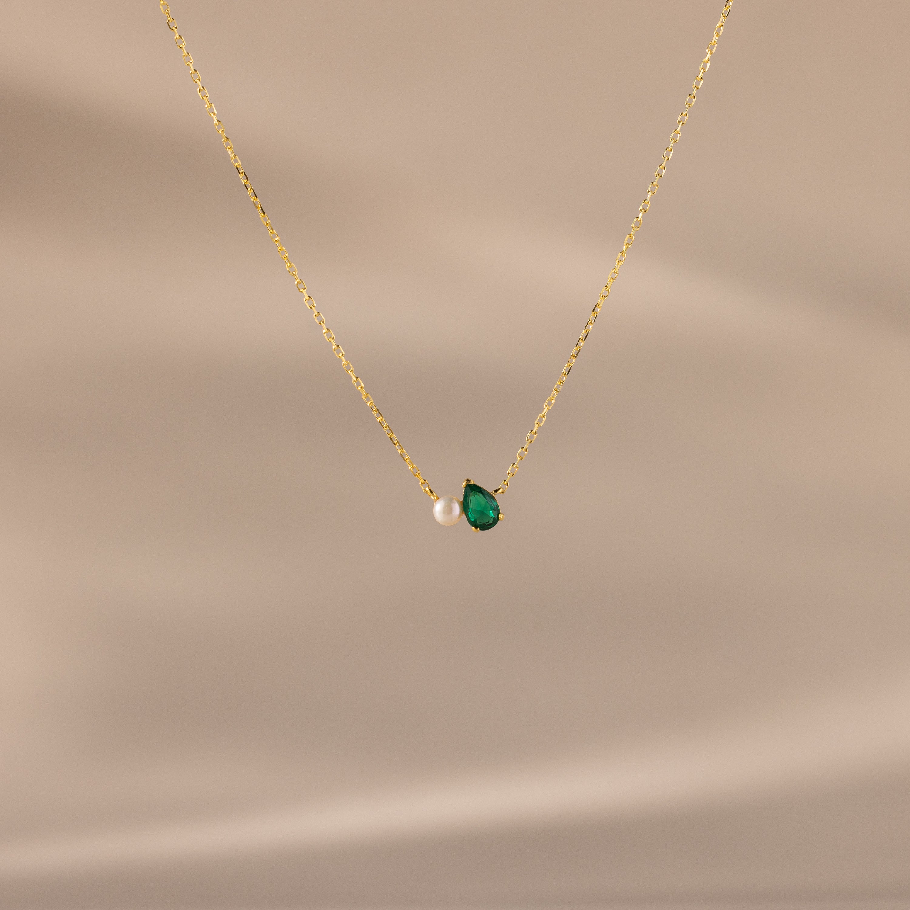 Teardrop Emerald & Pearl Necklace displayed on a beige background. This gold chain pearl necklace with a green teardrop pendant makes a timeless gift, perfect for any occasion.