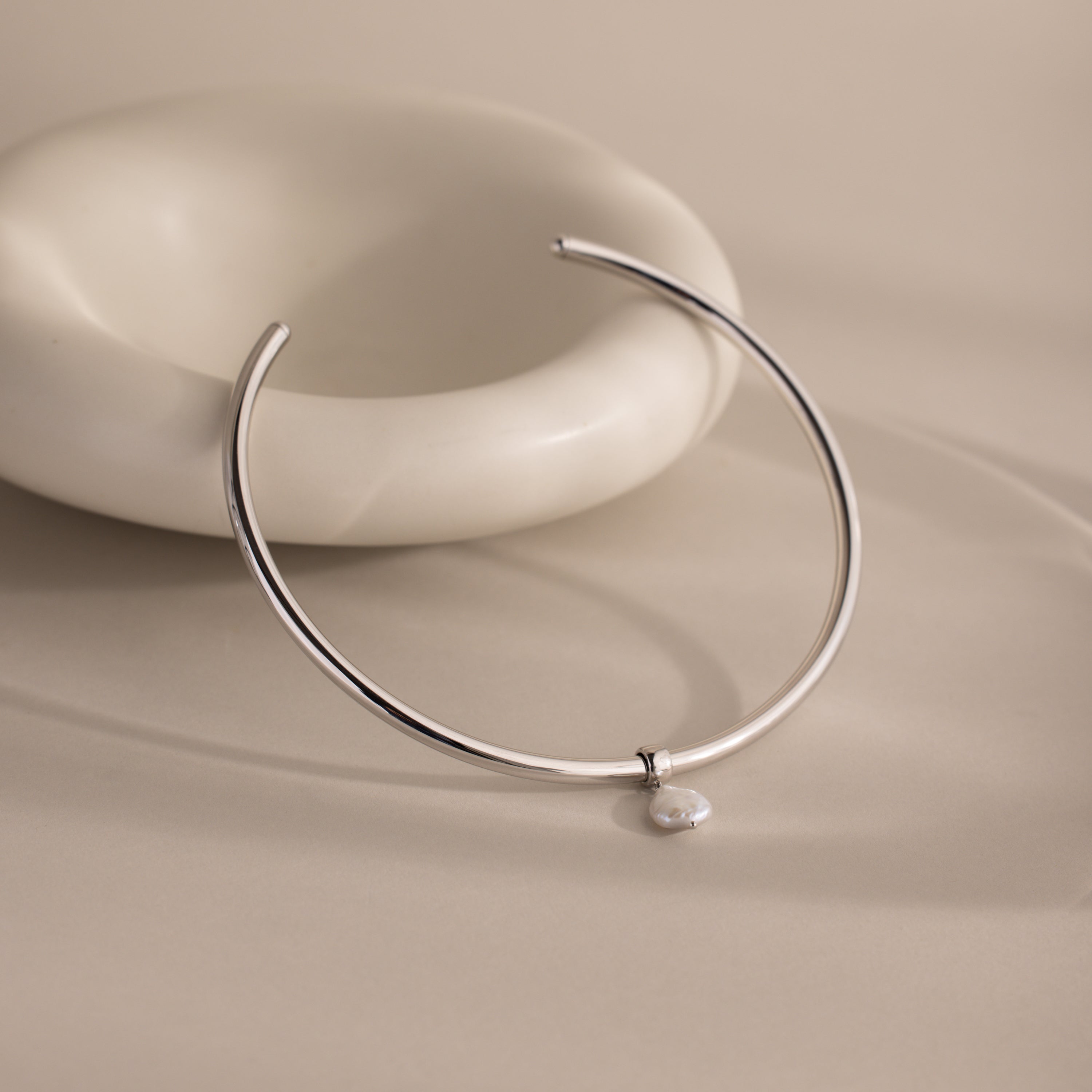 The Pearl Cuff Choker Necklace in White Gold features a stunning baroque pearl pendant and shines with timeless elegance against a beige backdrop.