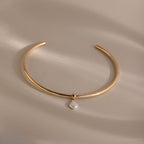 The Pearl Cuff Choker Necklace in 18K Gold features a small baroque pearl pendant, shown on a beige background with soft lighting.