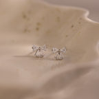 Close-up of silver bow stud earrings with clear crystal accents, displayed on a ceramic dish.