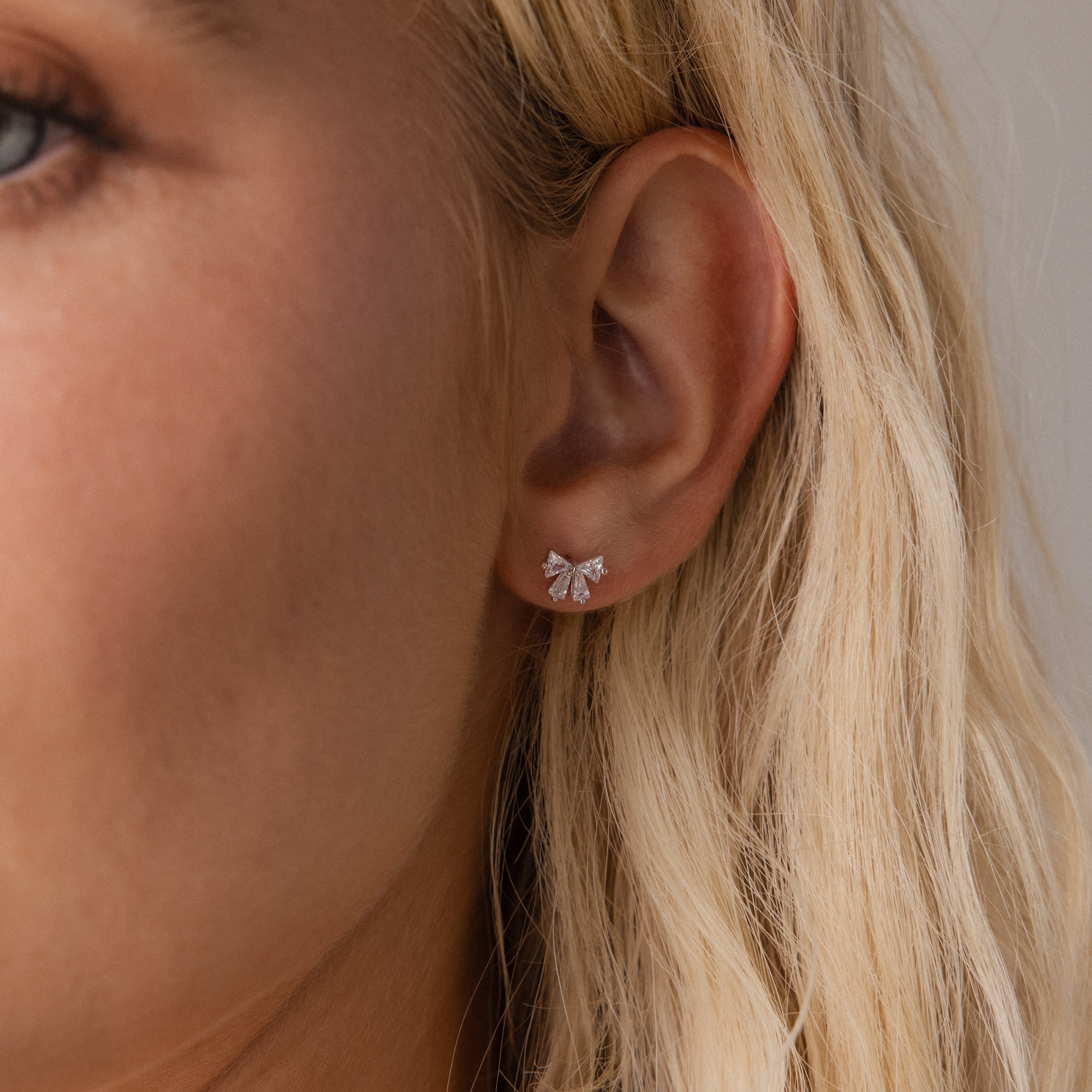 Close up of a woman wearing the Starlight Bow stud earring in silver, featuring baguette cut clear stones arranged in a delicate bow design for an elegant look.