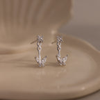 Close-up of silver butterfly jacket earrings with delicate crystal detailing, displayed on a cream ceramic dish.