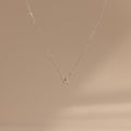 The Diamond Bow Necklace features a delicate gold-plated chain with a minimalist bow pendant, beautifully displayed on a soft beige background.