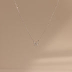 The Diamond Bow Necklace features a delicate gold-plated chain with a minimalist bow pendant, beautifully displayed on a soft beige background.