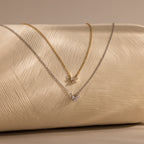 A delicate Diamond Bow Necklace in 18K Gold with a small bow-shaped pendant, displayed on a beige surface.