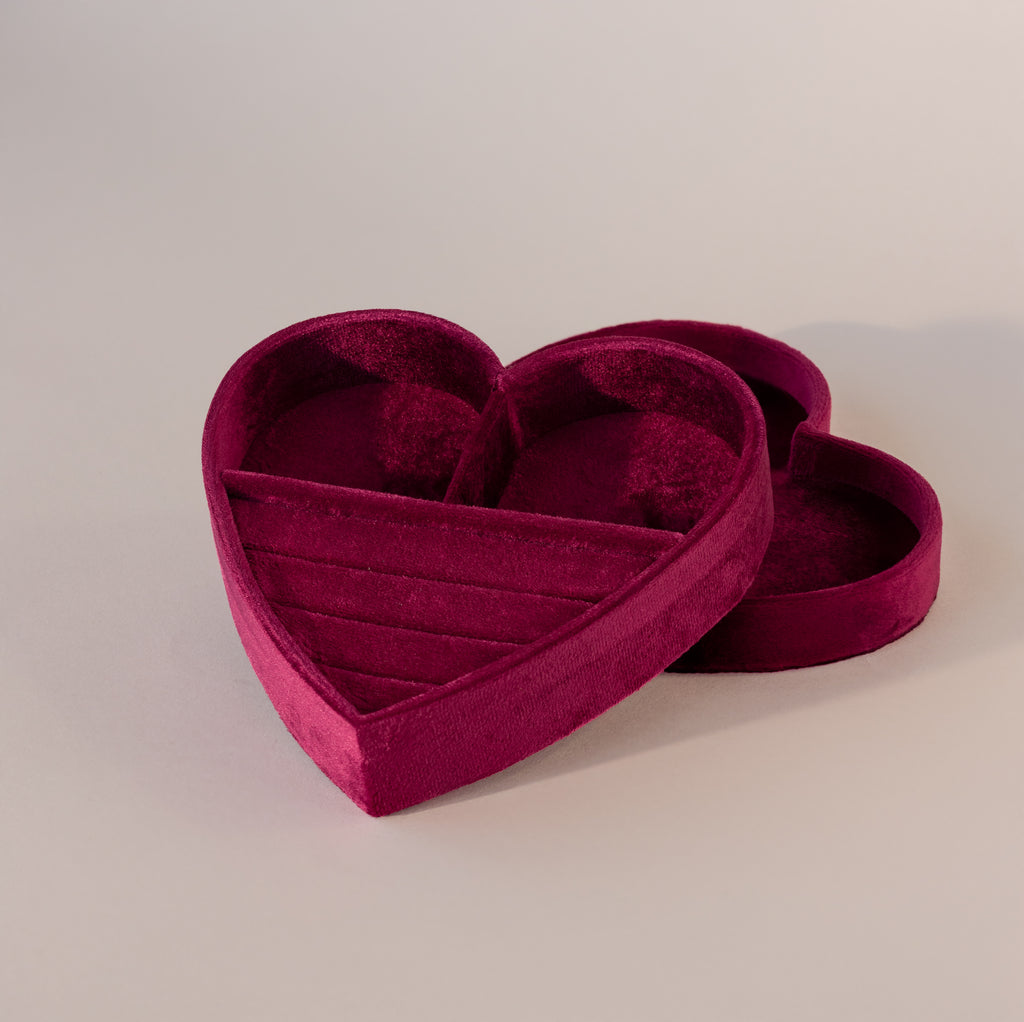 Red velvet heart-shaped jewelry box with lid, featuring ring slots and compartments on a neutral background.