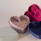 Velvet heart-shaped jewelry boxes in lavender, red, blue, and mint green, with the lavender box open to display gold rings, bracelet, and necklace.