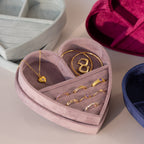 Velvet heart-shaped jewelry box in lavender filled with gold rings, a heart pendant necklace, and bangles, displayed alongside other colorful velvet boxes.