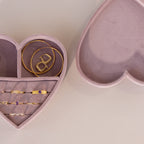 Open lavender velvet heart-shaped jewelry box with gold rings and bracelets neatly displayed inside, shown beside its matching lid on a neutral background.