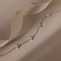 Delicate silver necklace with floral pendants on a soft beige fabric background