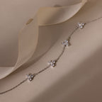 Delicate silver necklace with floral pendants on a soft beige fabric background