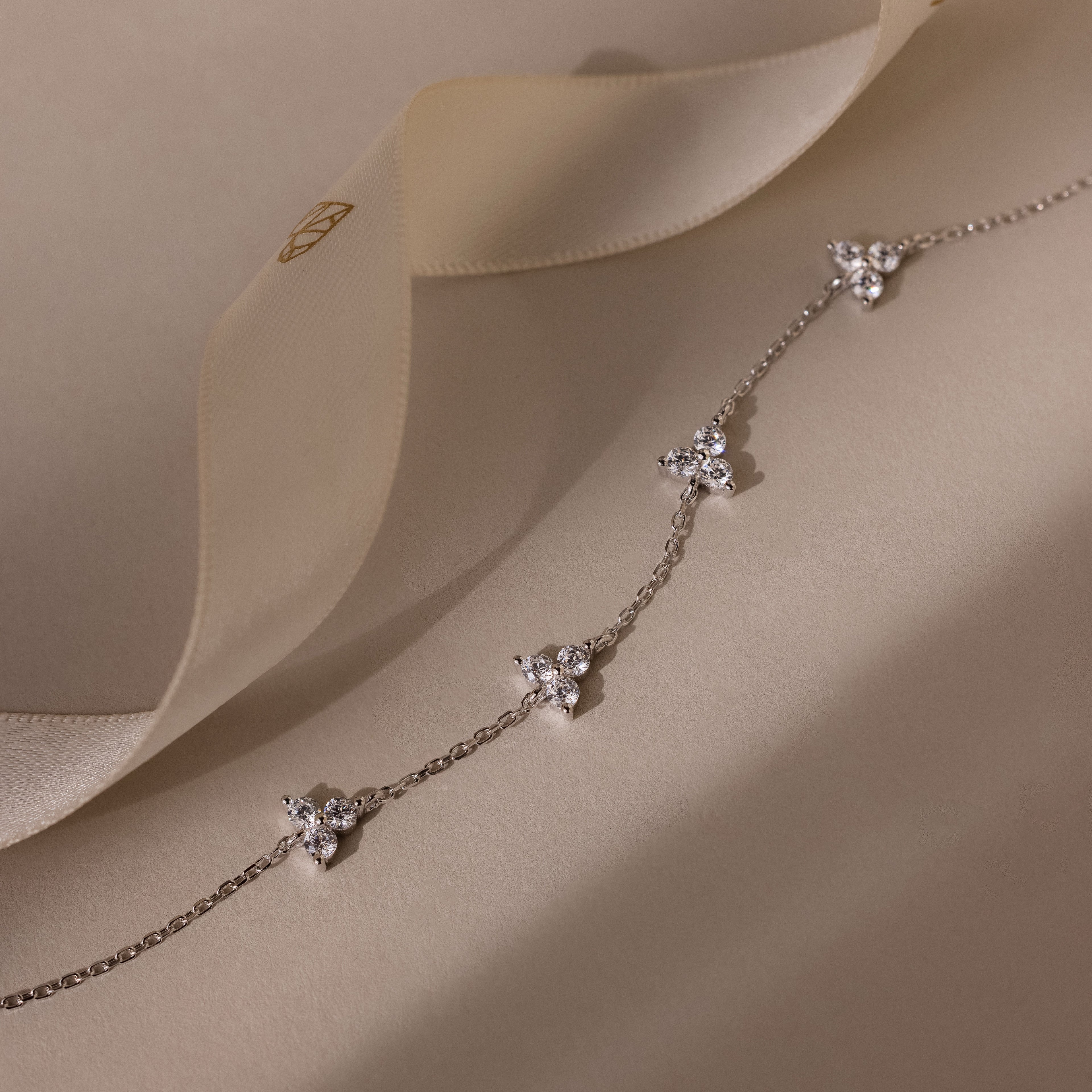 Delicate silver necklace with floral pendants on a soft beige fabric background