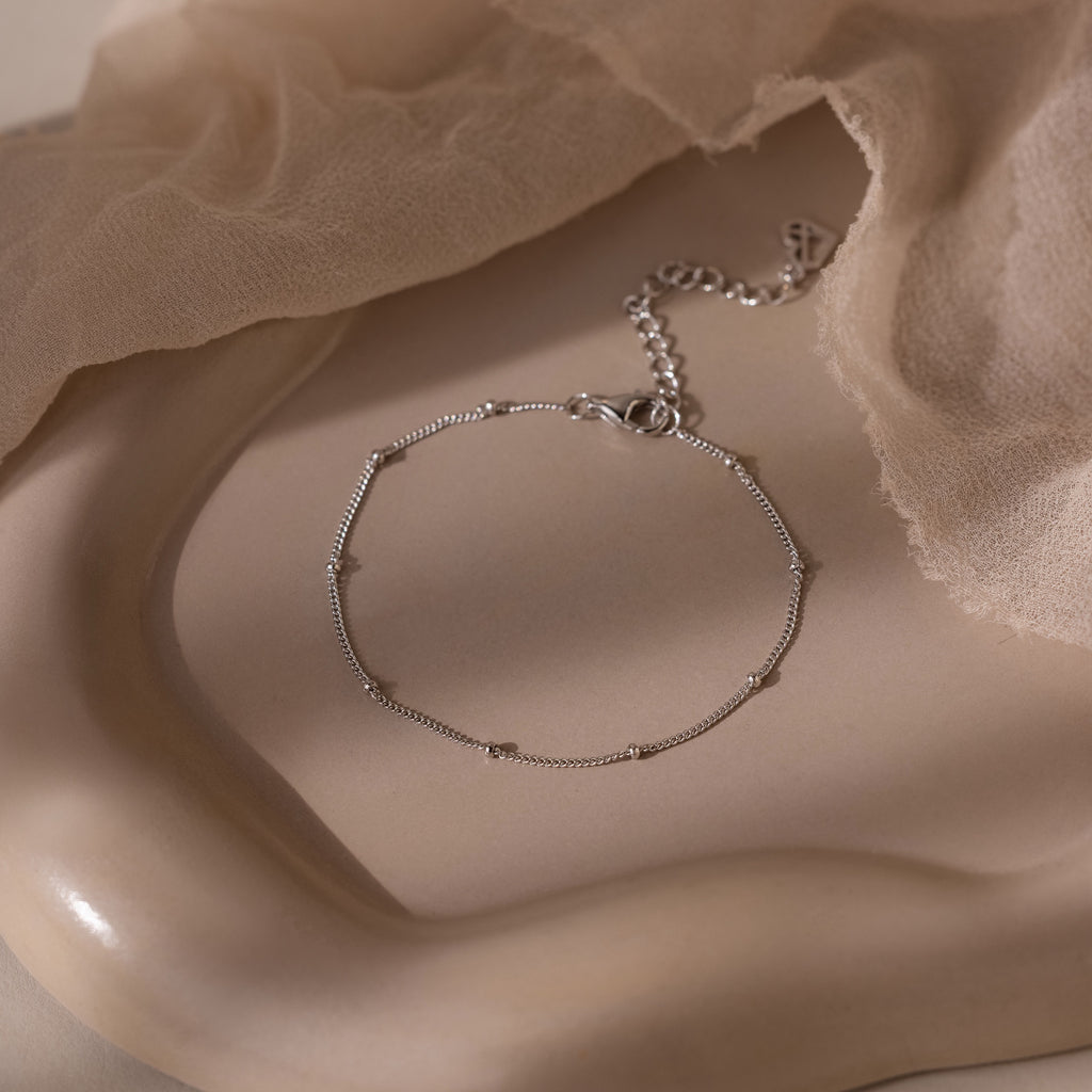 Silver beaded bracelet on a soft beige stone background