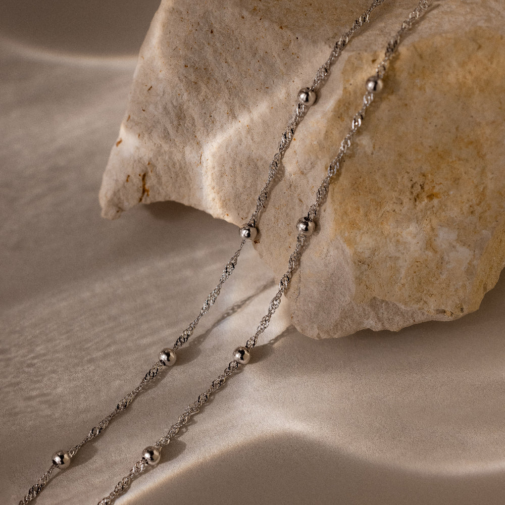 Two silver beaded bracelets draped over a textured stone surface
