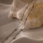 Two silver beaded bracelets draped over a textured stone surface
