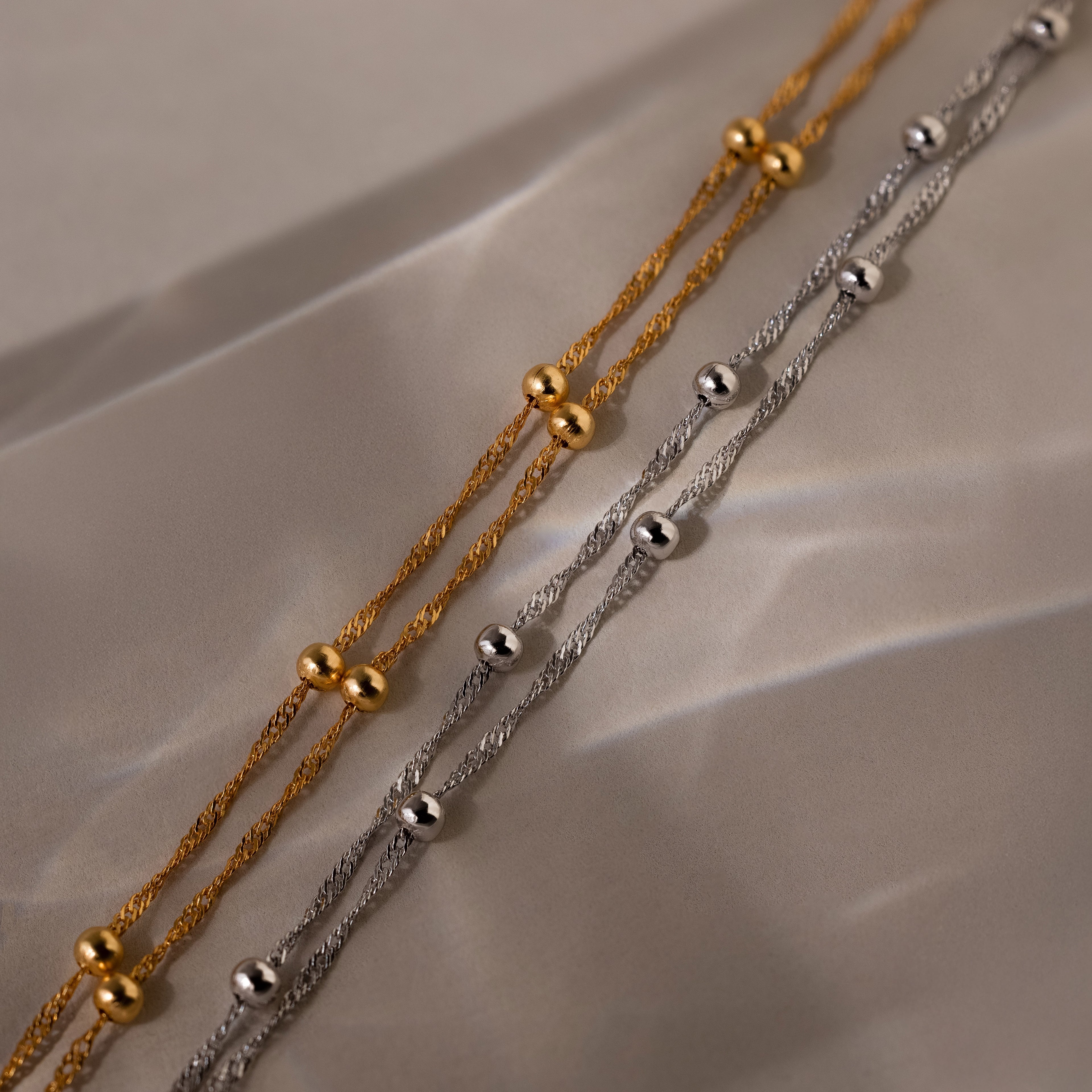 Two gold and silver beaded necklaces on a beige fabric background