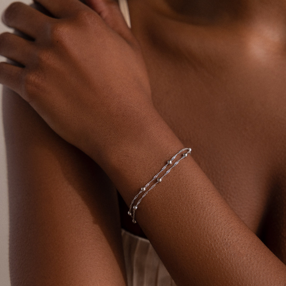 Silver beaded bracelet on a person's wrist with a neutral background