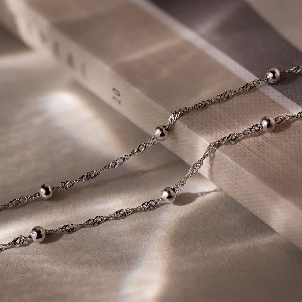 Silver double chain anklet with beads on a textured surface