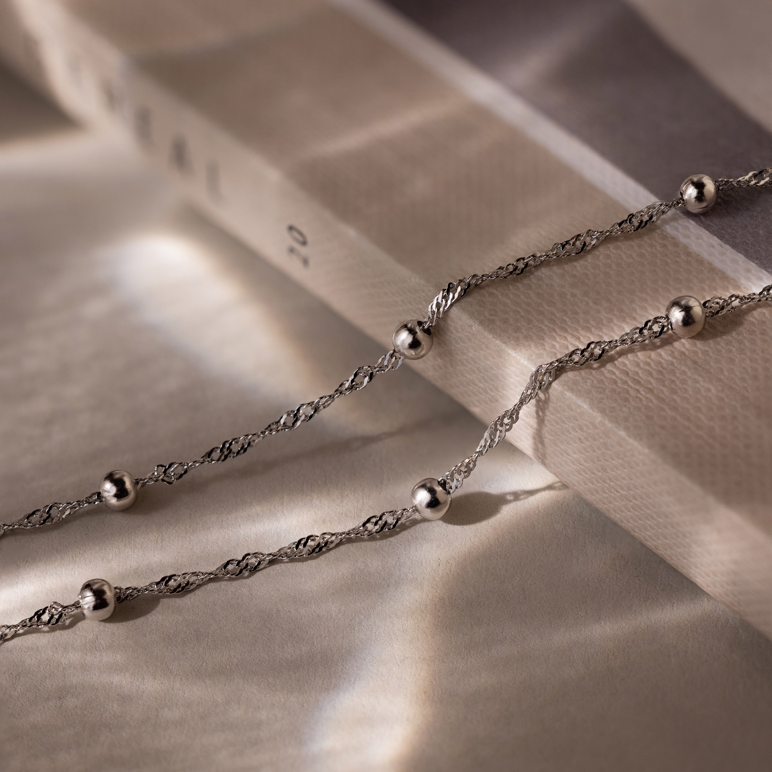 Silver double chain anklet with beads on a textured surface