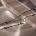 Silver double chain anklet with beads on a textured surface