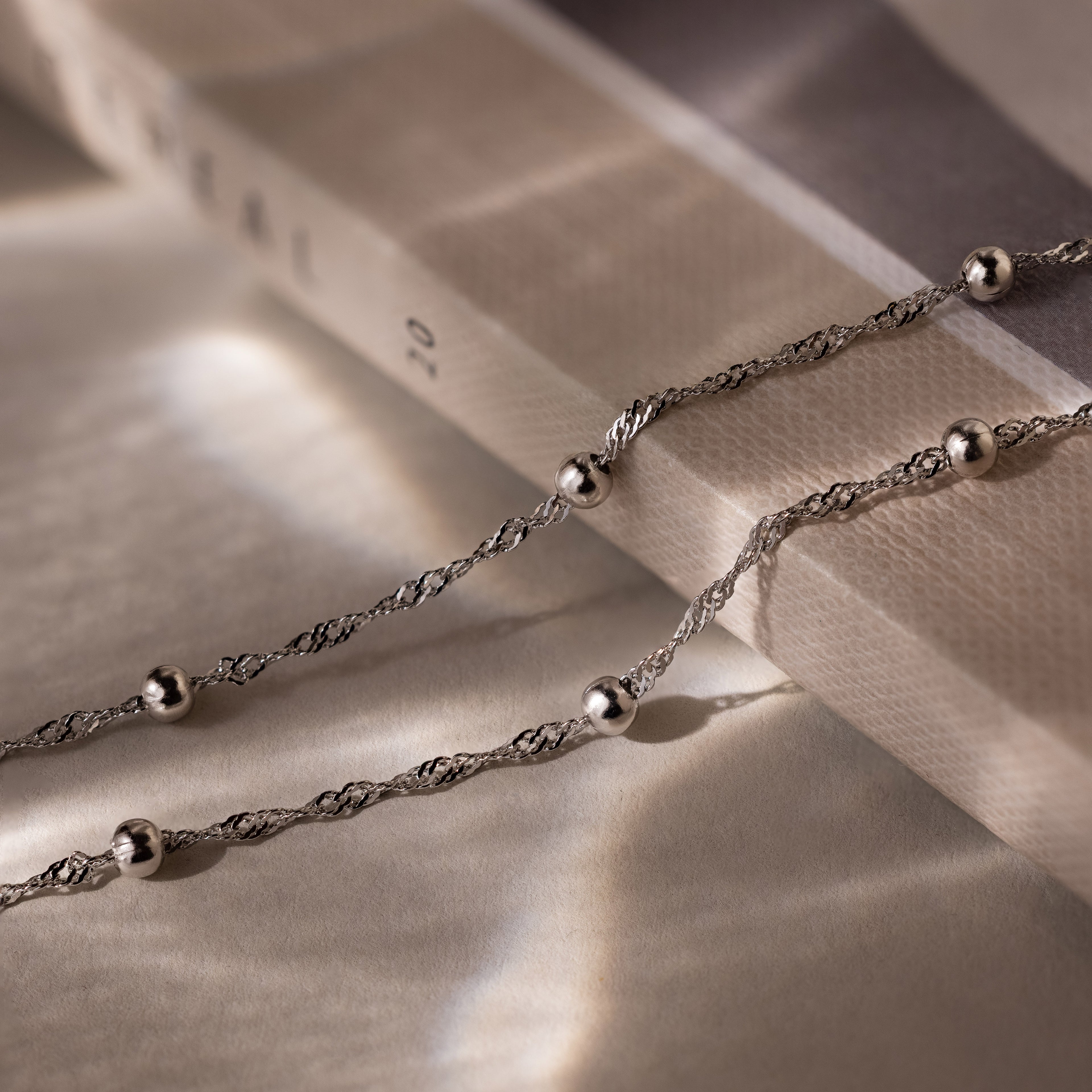 Silver double chain anklet with beads on a textured surface