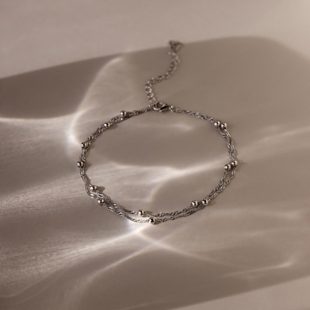 Silver beaded anklet on a textured beige surface
