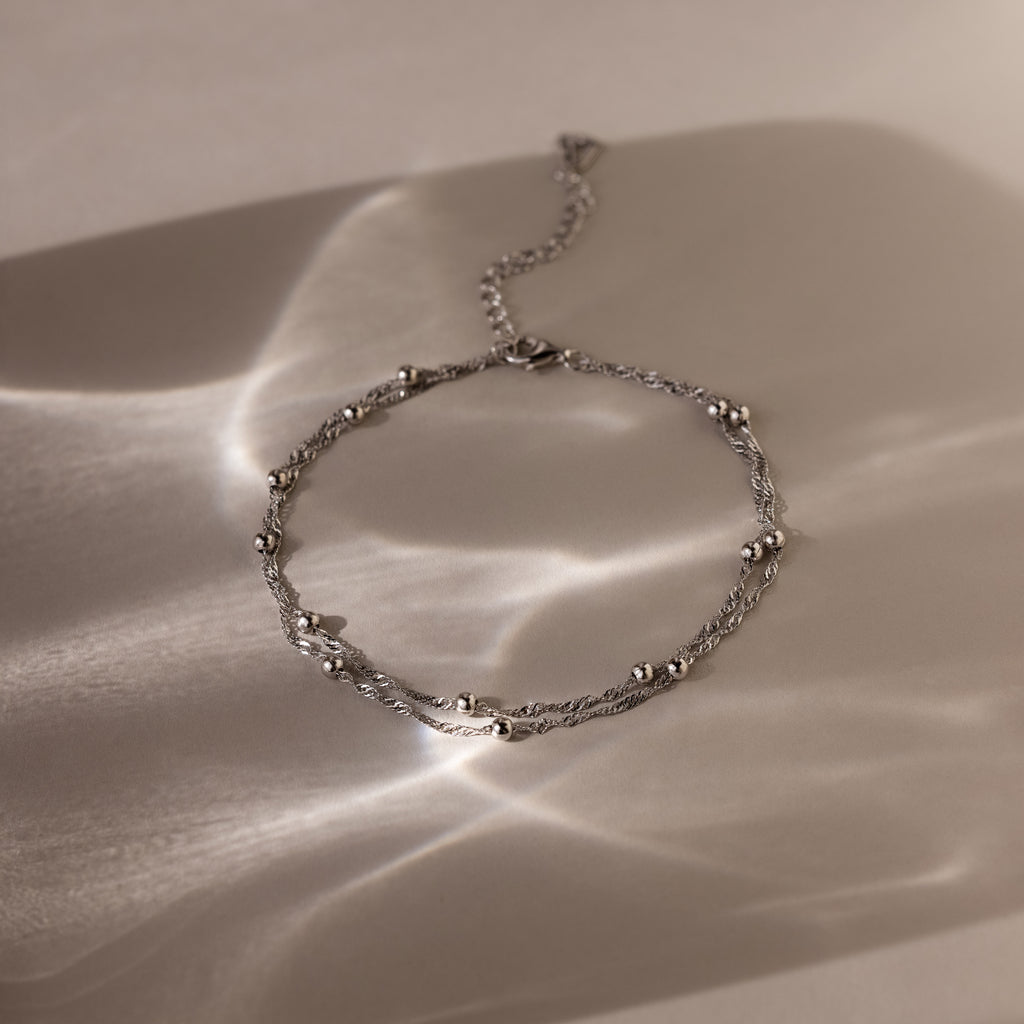 Silver Beaded Anklet on a textured beige surface