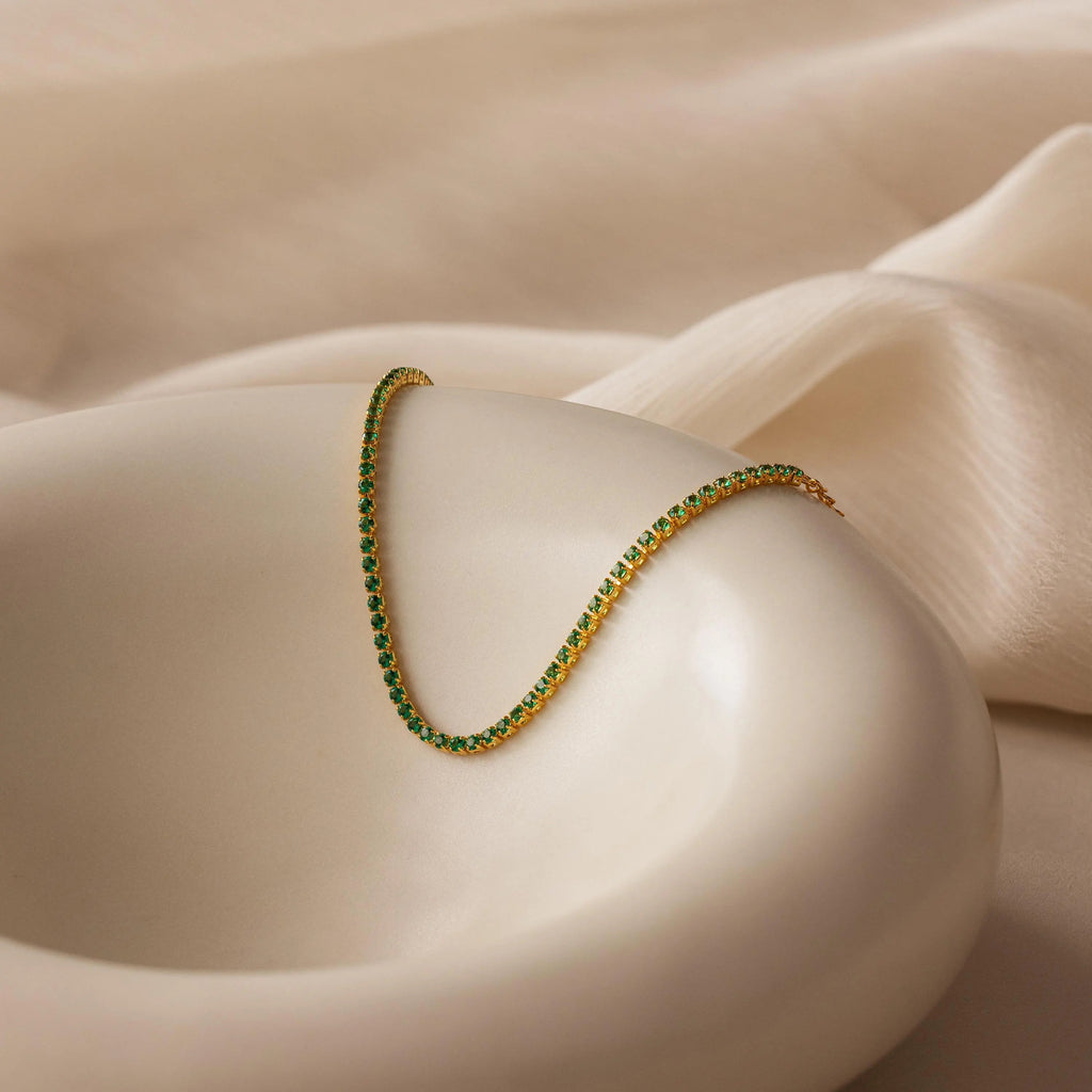 Classic Birthstone Tennis Bracelet showcased on a smooth white dish against a soft beige fabric background, ideal for pairing with a gold necklace or other personalized jewelry.