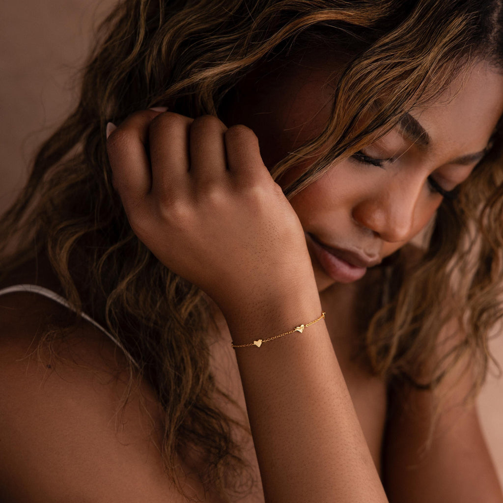 A woman with wavy hair gazes downward, wearing the Heart Station Bracelet. The delicate piece adds a romantic and graceful touch to her style.