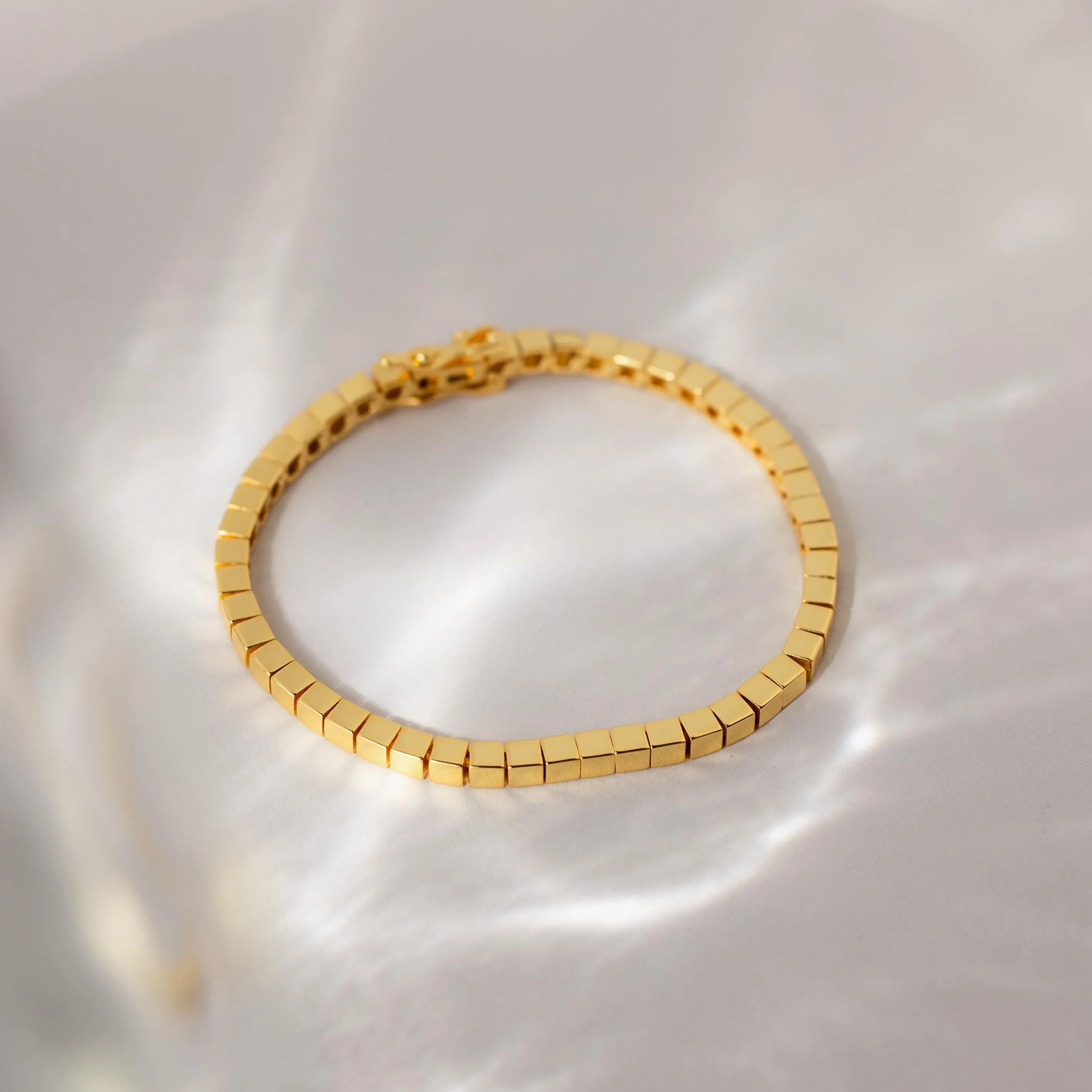 The Cube Bracelet features geometric bead links and rests on a light, reflective surface, casting soft shadows—a bold men's statement jewelry piece.